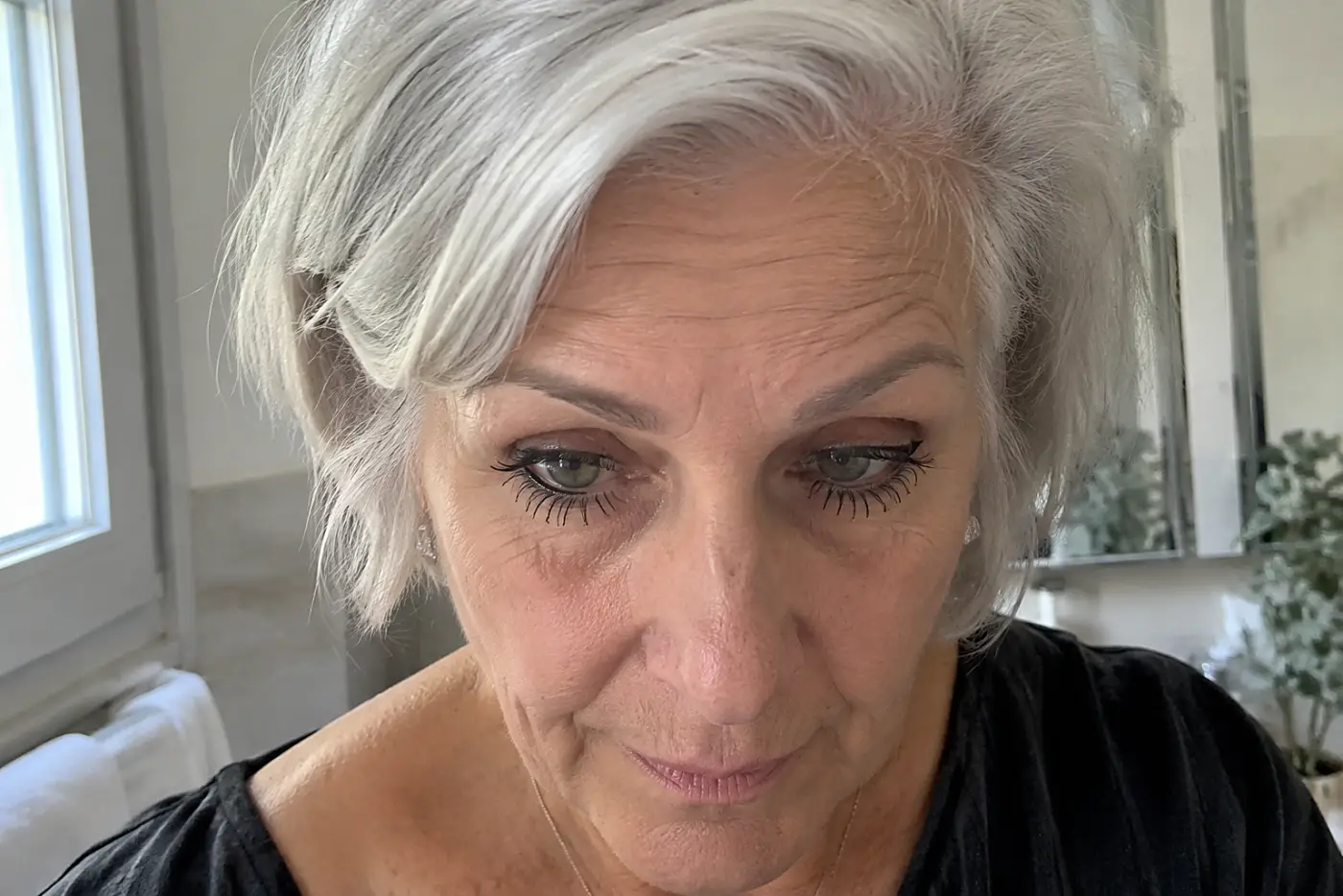 A woman in her sixties with grey hair wears heavy mascara on her lower lashes.