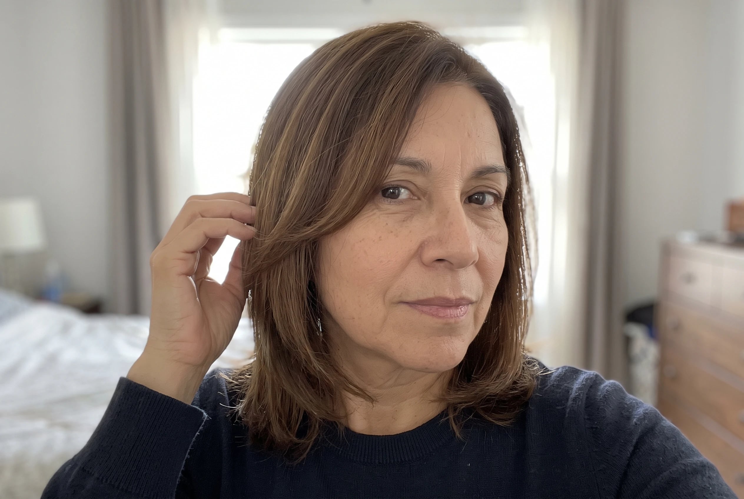 A woman in her sixties adjusts her shoulder-length brown hair with face-framing layers.