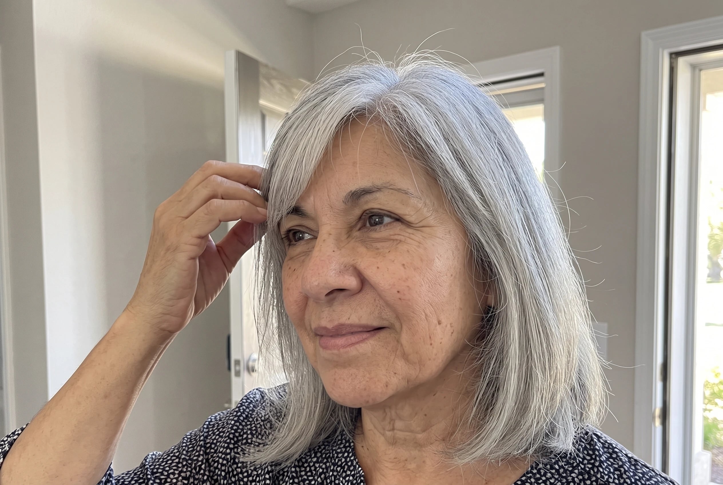 A woman in her sixties adjusts her shoulder-length silver hair with swooping side bangs.