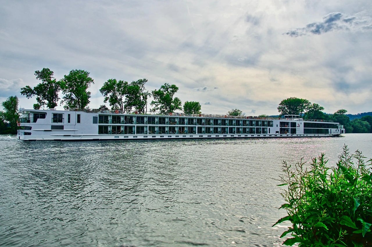 Long white river cruise ship with balcony cabins sailing along a calm river lined with trees