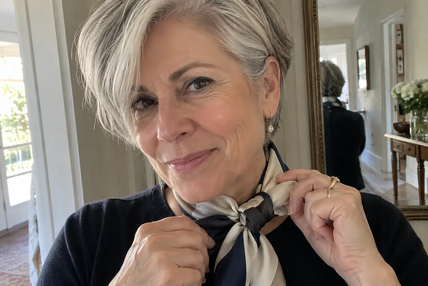 A woman with short grey hair adjusts a silk scarf tied tightly around her neck.