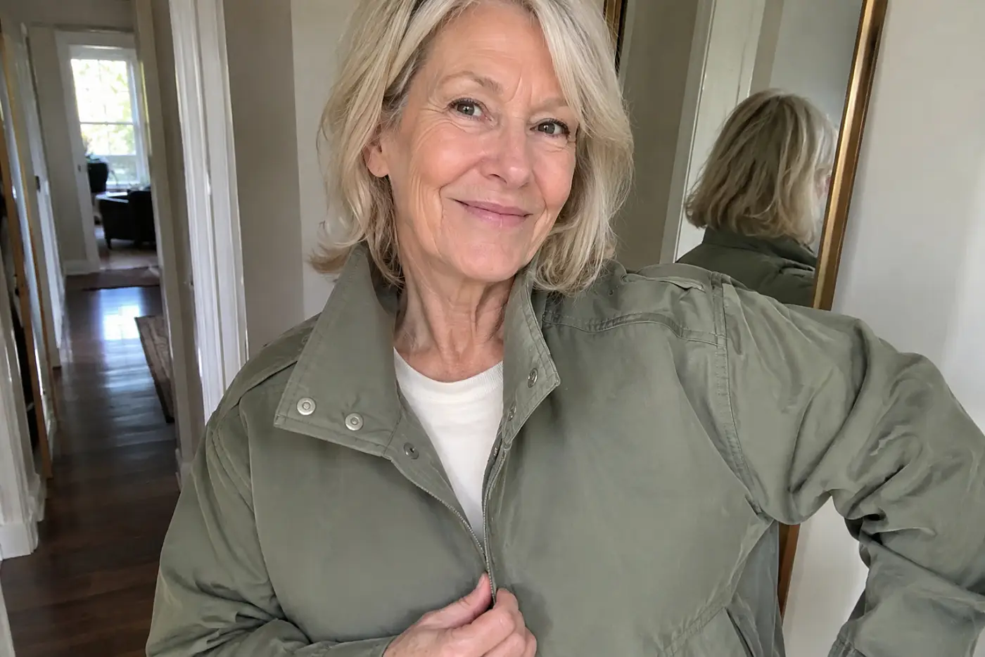 A woman in her sixties wears an olive green jacket with dropped shoulders at home.