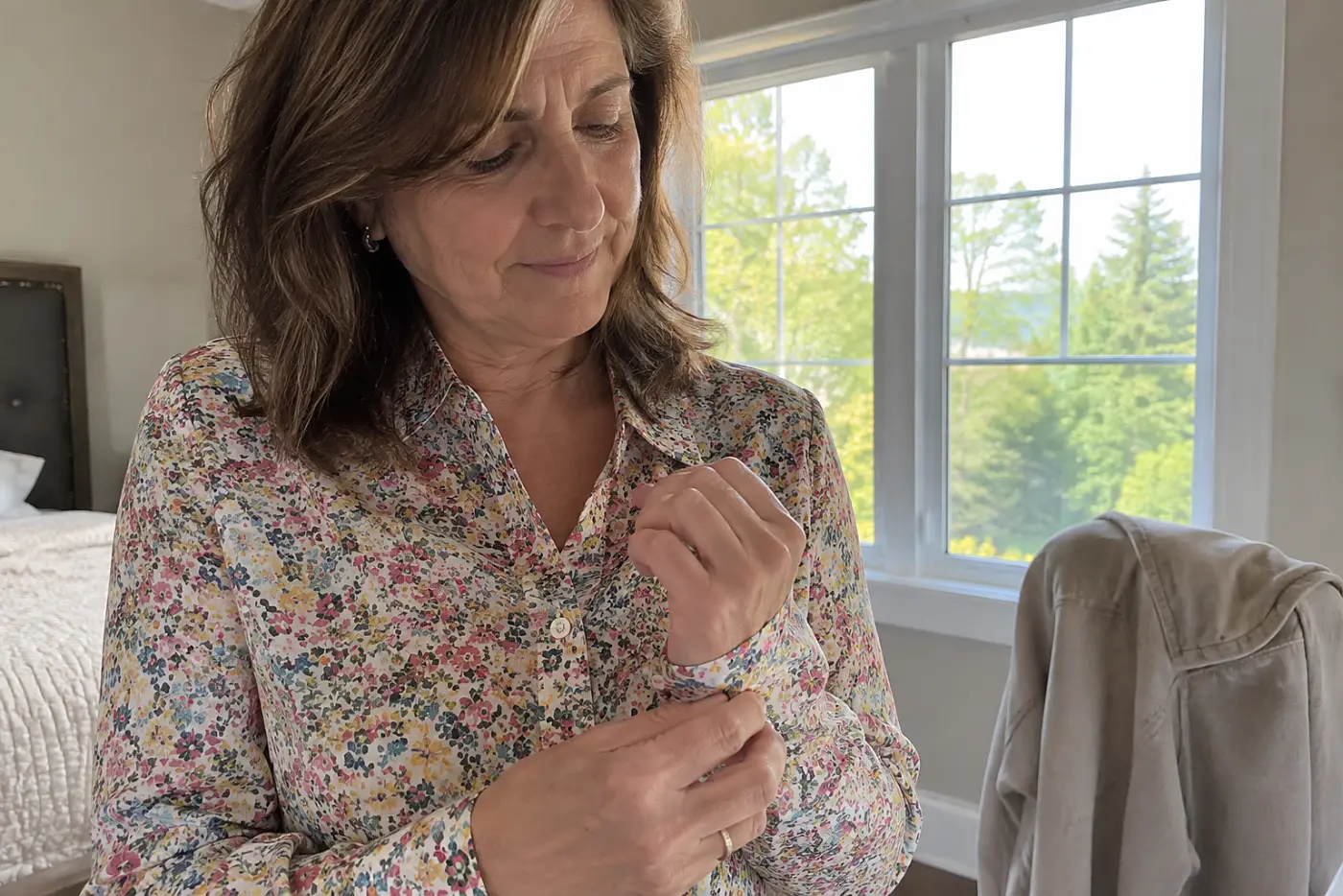 A woman in her fifties buttons the cuff of a tiny floral print blouse.