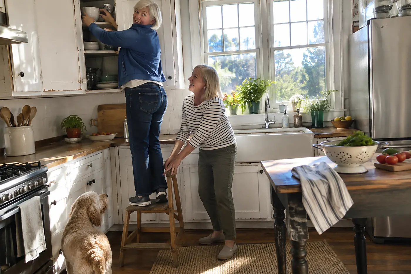 A woman in her sixties reaches into a kitchen cabinet, her blue jacket riding up.