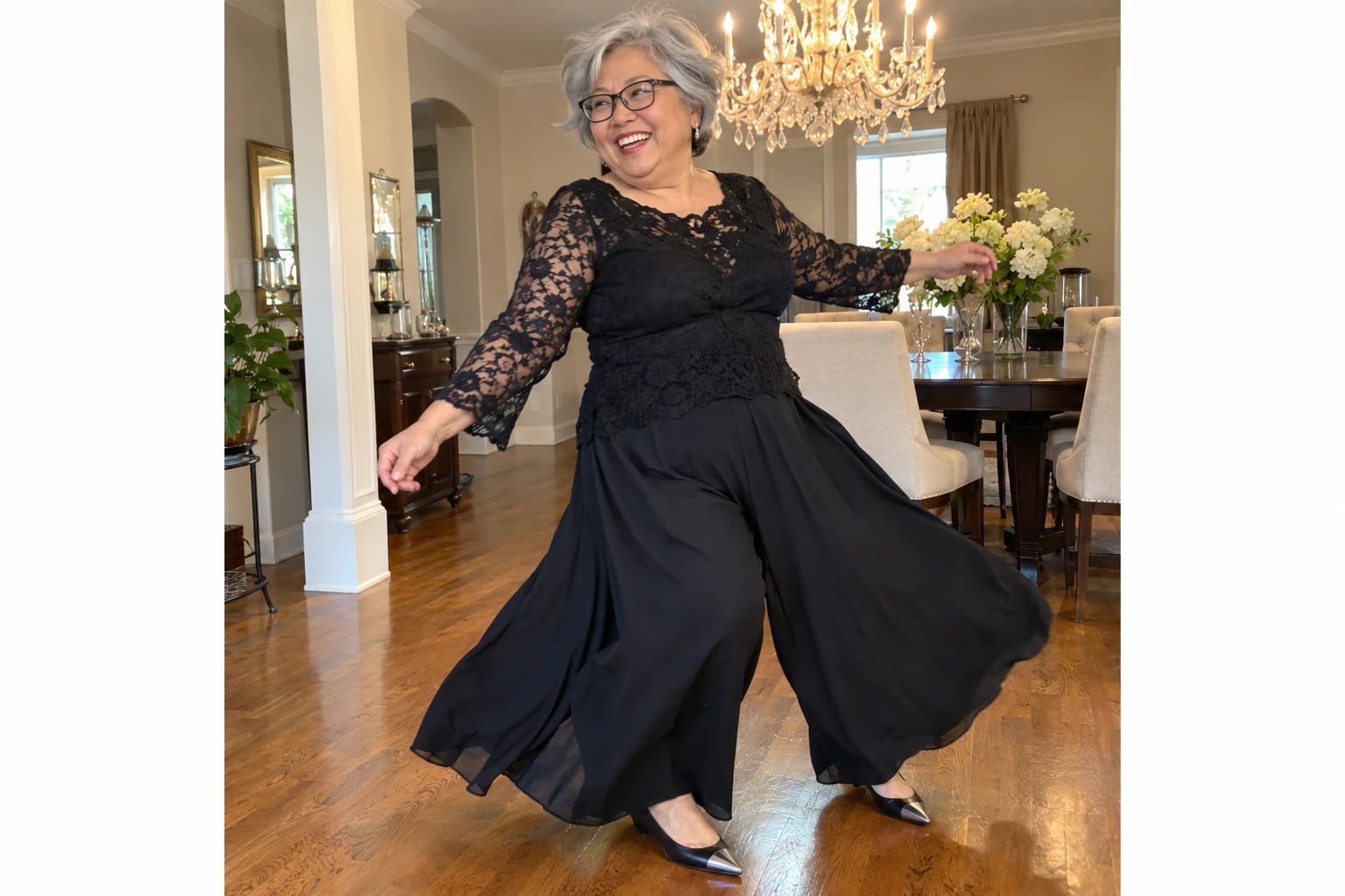 A smiling plus-size woman in her sixties twirls in a black lace top and flowing palazzo pants beneath a chandelier.