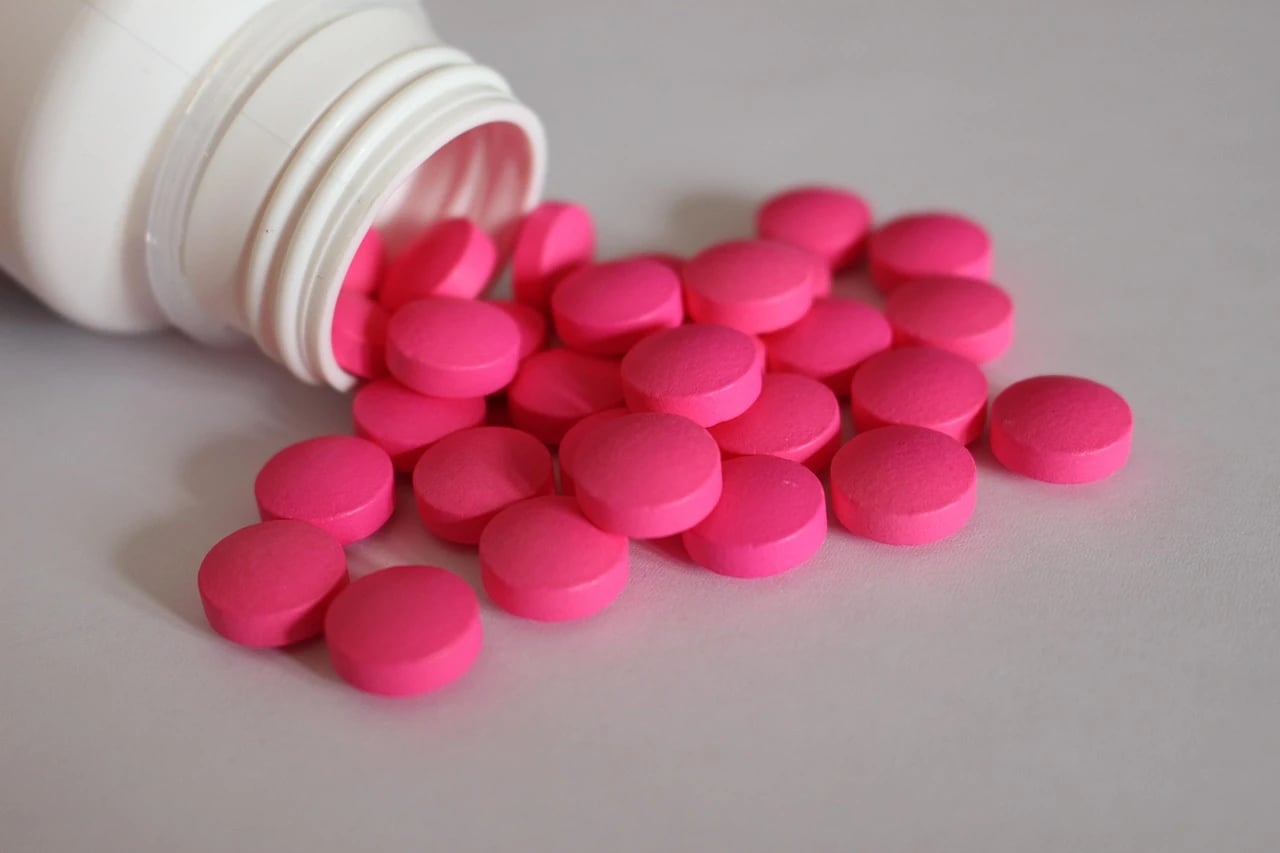 White pill bottle tipped on its side with many pink round tablets spilled across a light surface