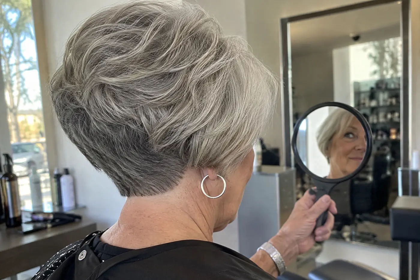 Woman viewing the stacked back of her gray wedge in a salon hand mirror.