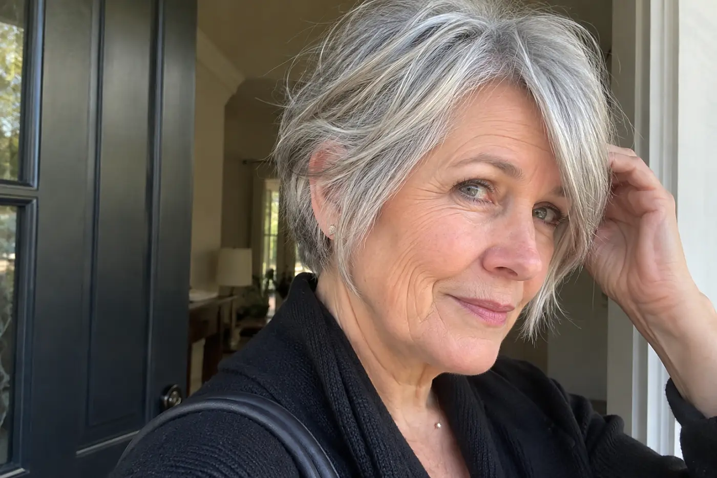 Woman smoothing an air-dried gray pixie bob before leaving her front door.