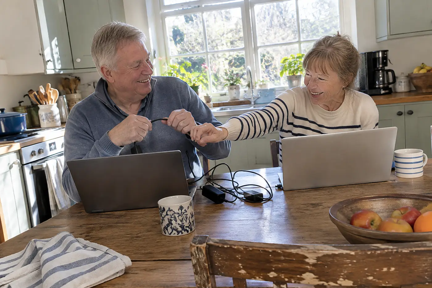 Married couple opening separate retirement accounts on laptops at their kitchen table.