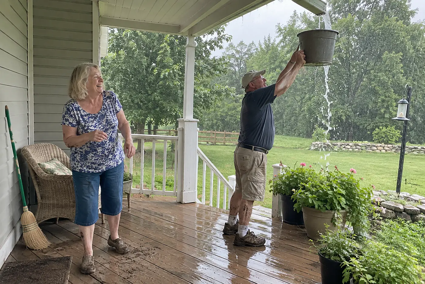 Older woman watching rain spill over a gutter from her back porch.