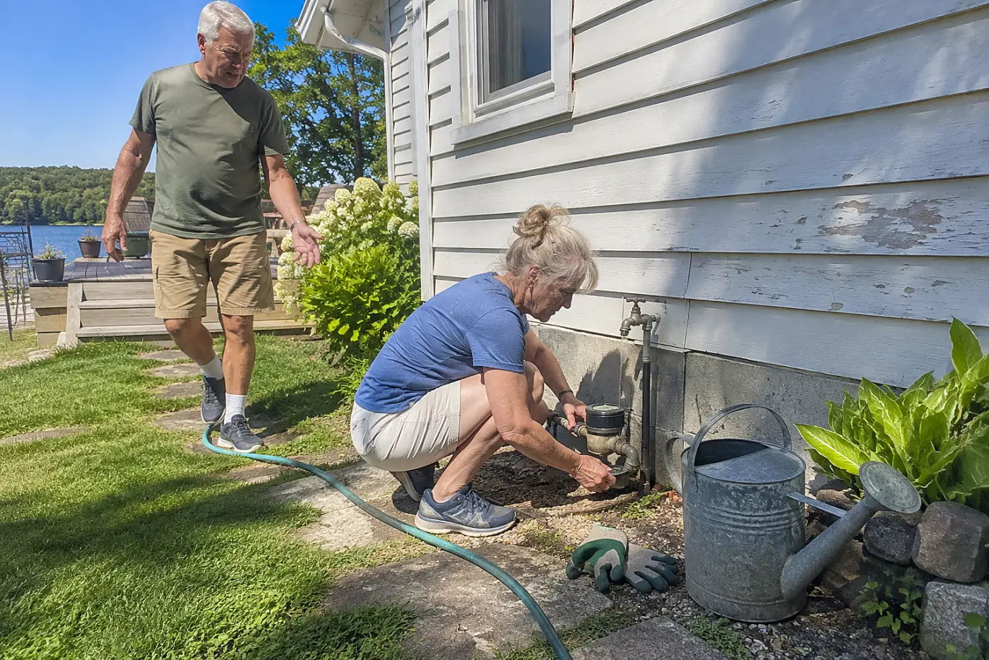 Older woman reading a water meter beside her house.