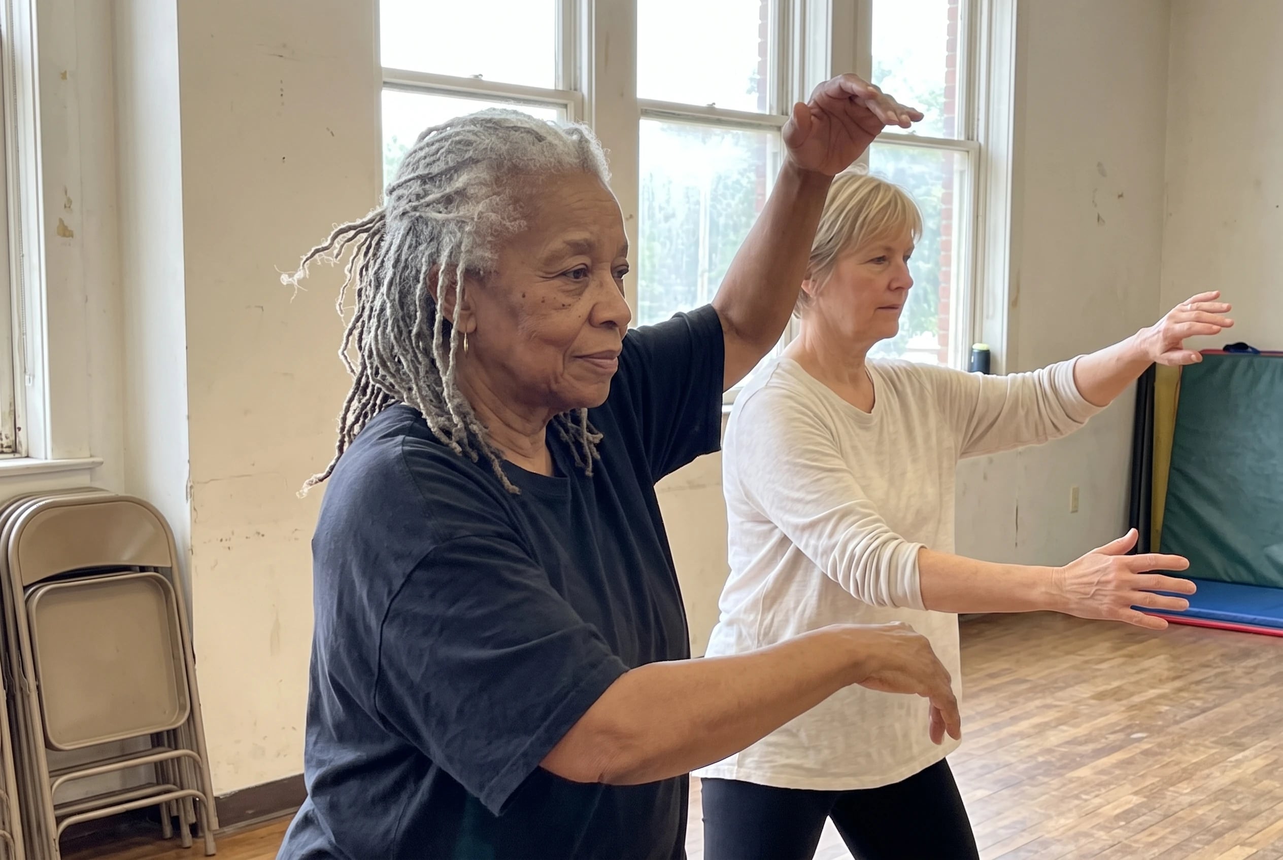 Woman following a tai chi instructor in a community center class.