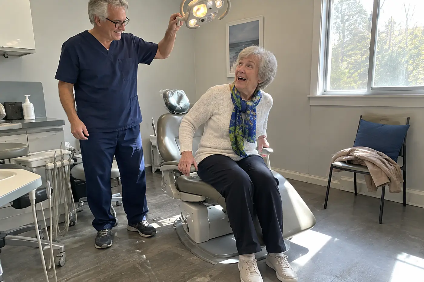 A woman in her 70s smiles from a dental chair as a dentist adjusts the light.