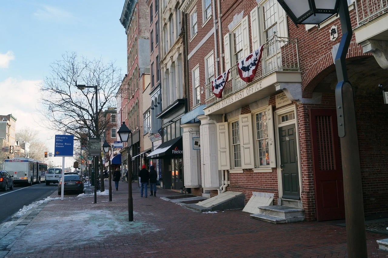 Brick sidewalk in Old City Philadelphia with pedestrians, historic post office building, shops, street lamps and a city bus
