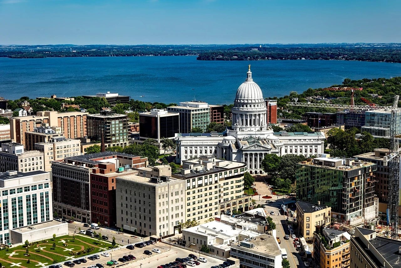 Aerial view of downtown Madison with the Wisconsin State Capitol dome, nearby buildings and streets, and the lake behind