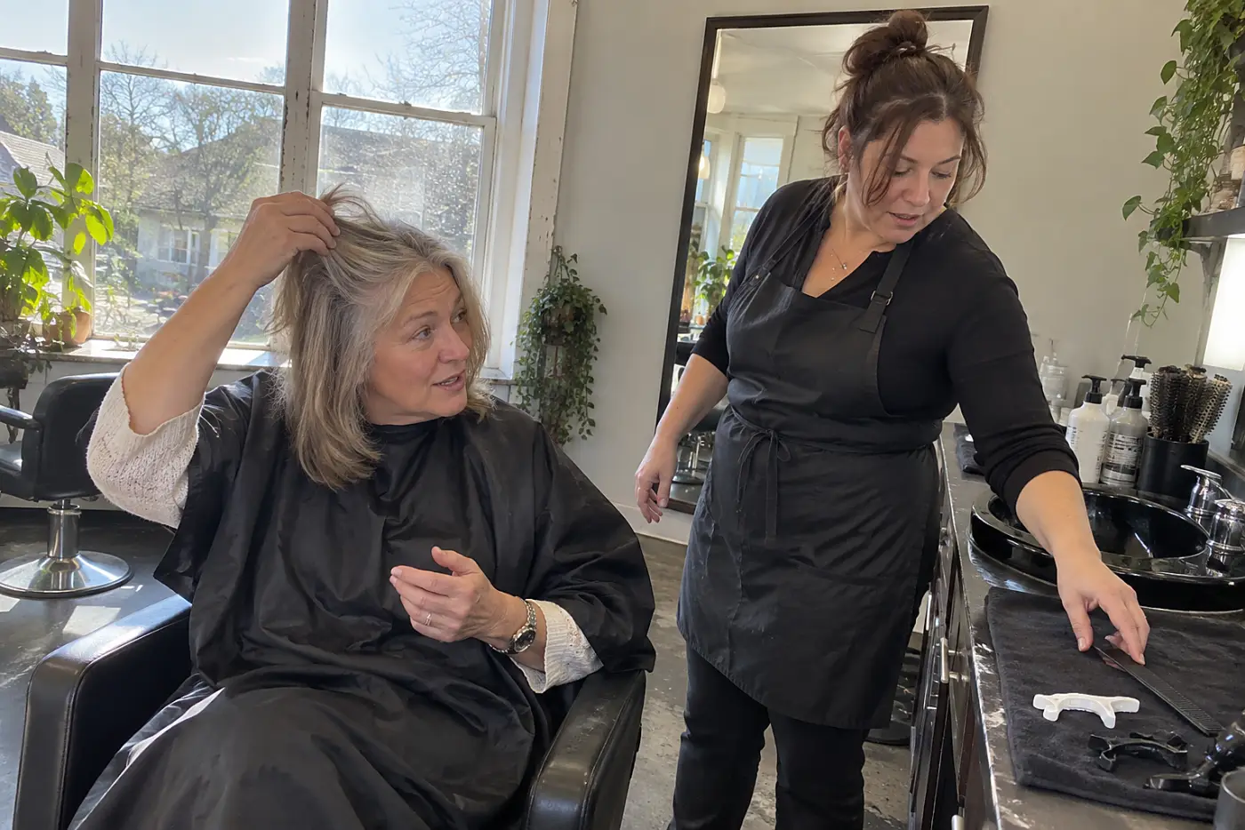 Older woman showing her gray roots to a stylist in a salon.
