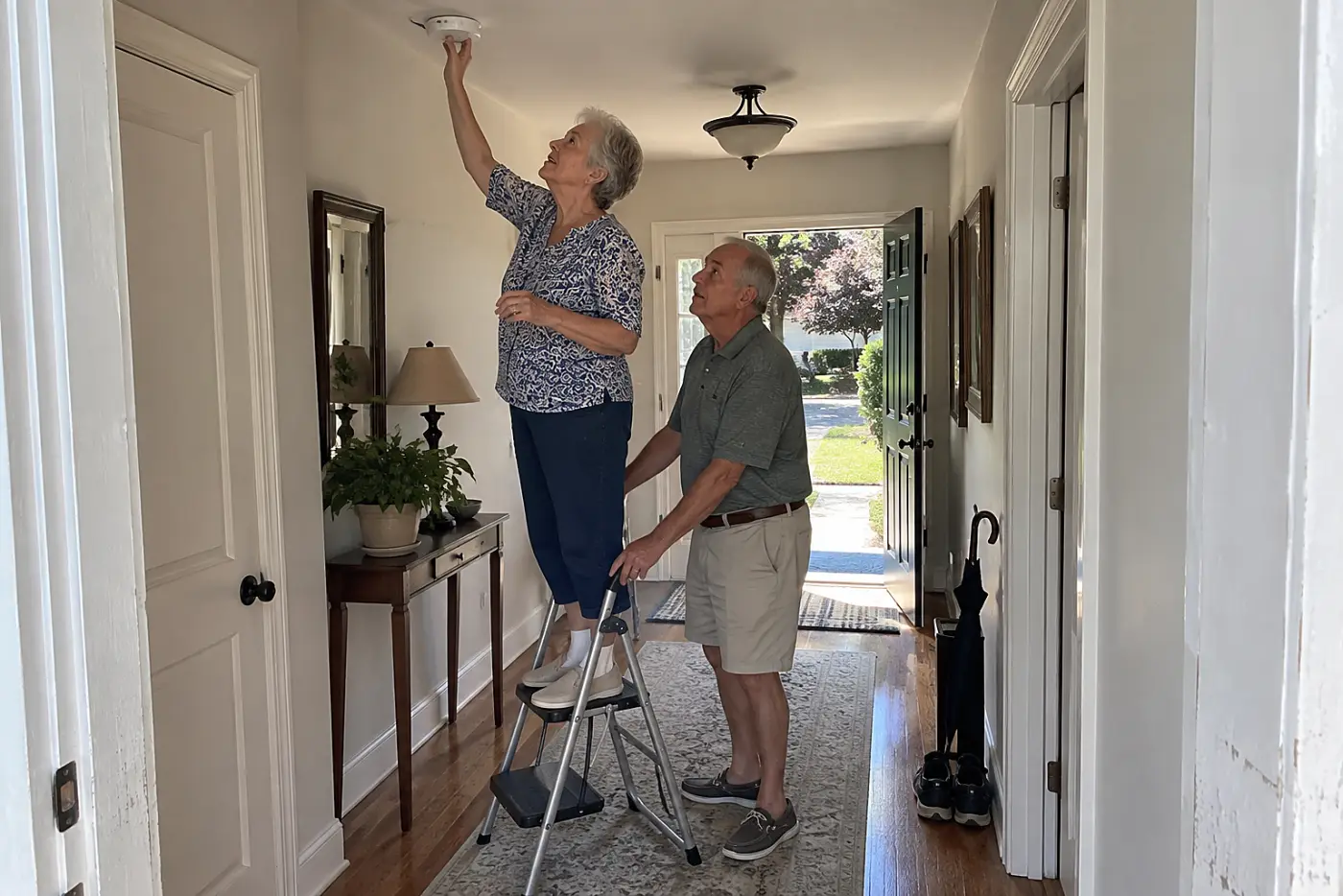 Older woman checking a smoke alarm in her hallway.