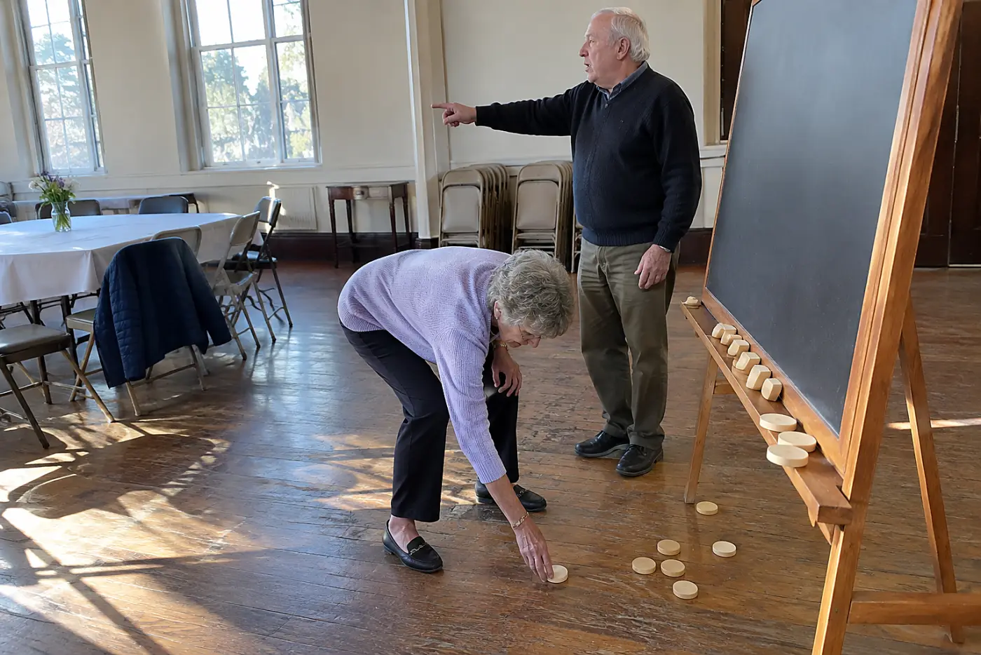 A woman in her seventies reviewing a volunteer shift list with an organizer in a community hall.