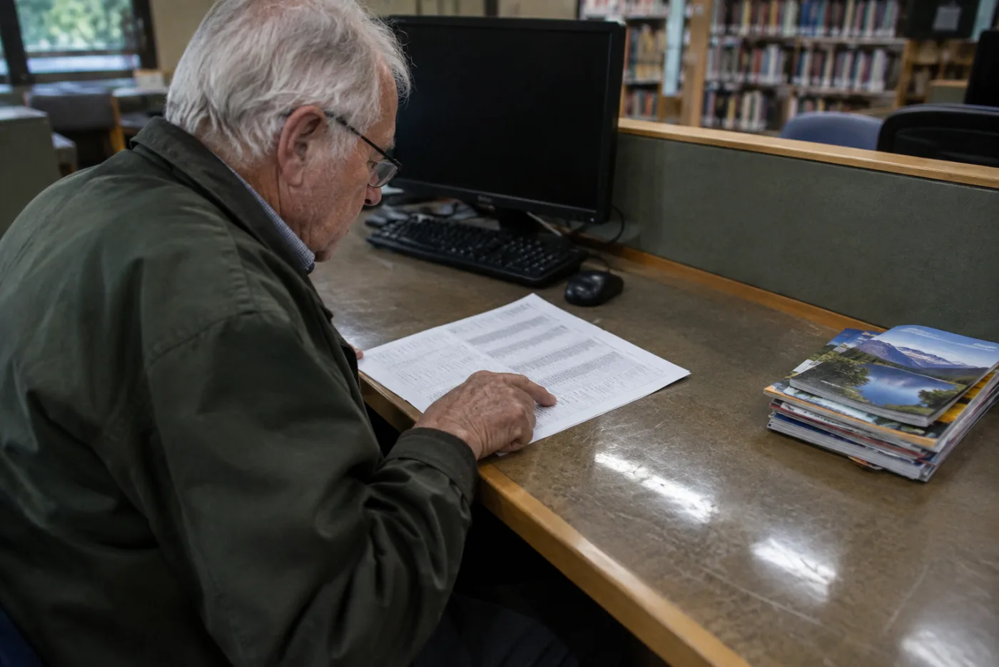 Man reviewing a printed list of plans at a library computer desk