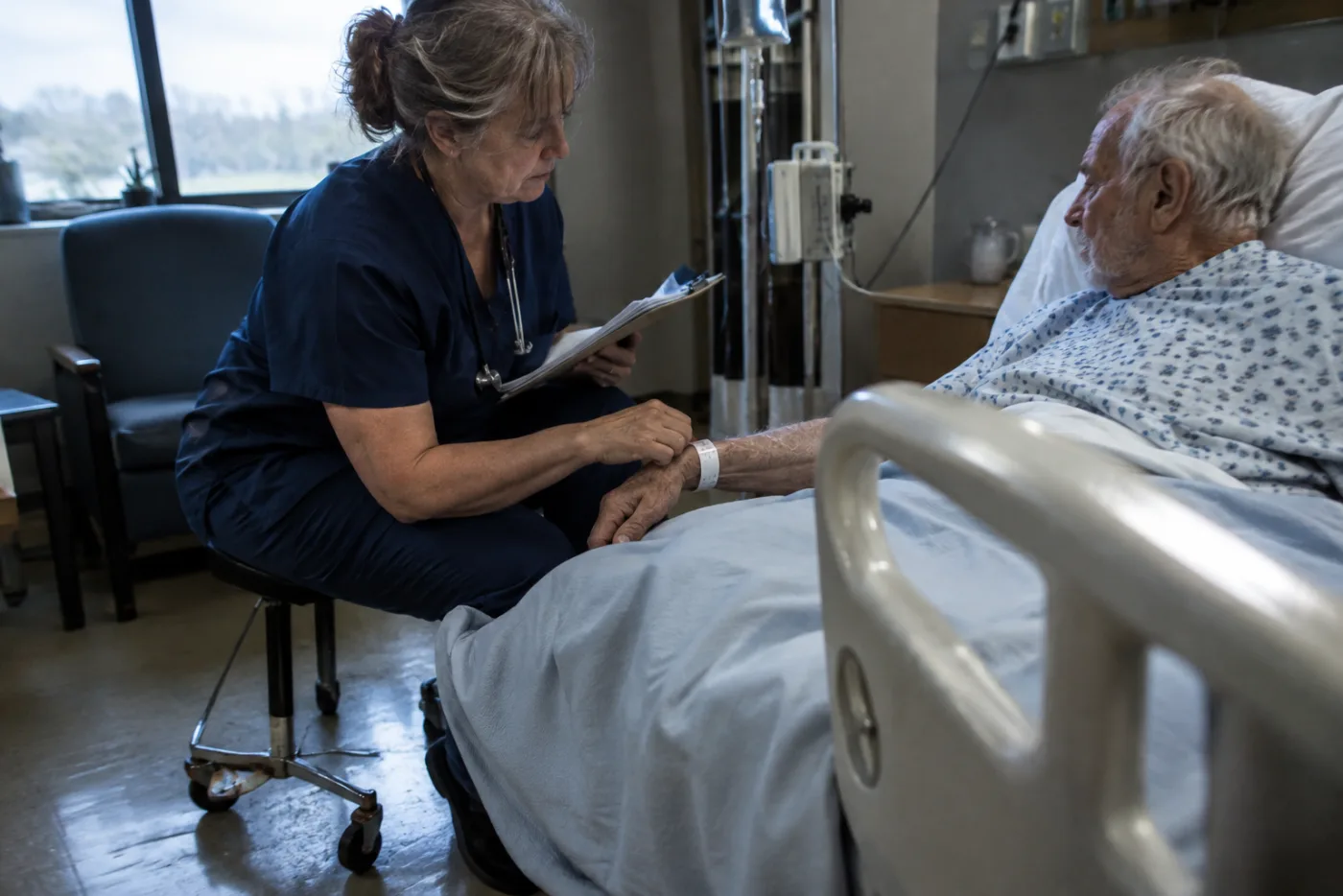 Nurse adjusting a patient's wristband while checking a clipboard in a hospital room