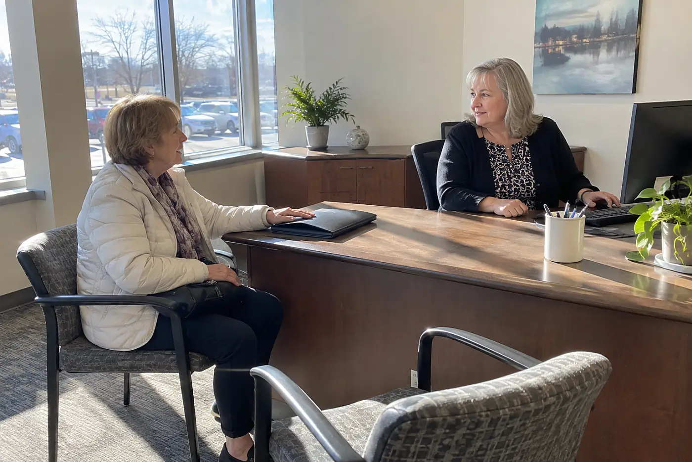 Older woman speaking with a bank employee across a branch desk.