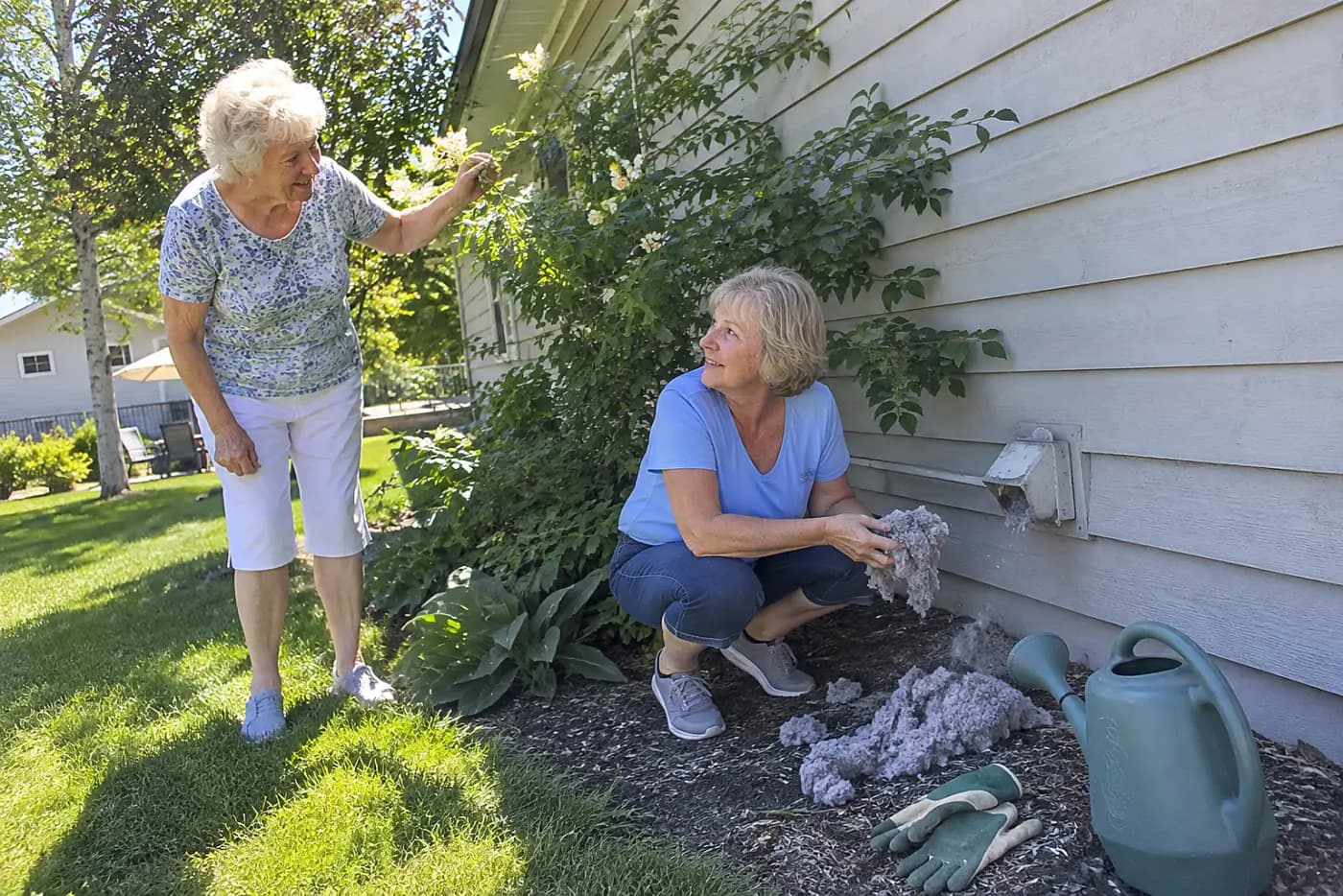 Older woman checking the outdoor dryer vent beside her house.