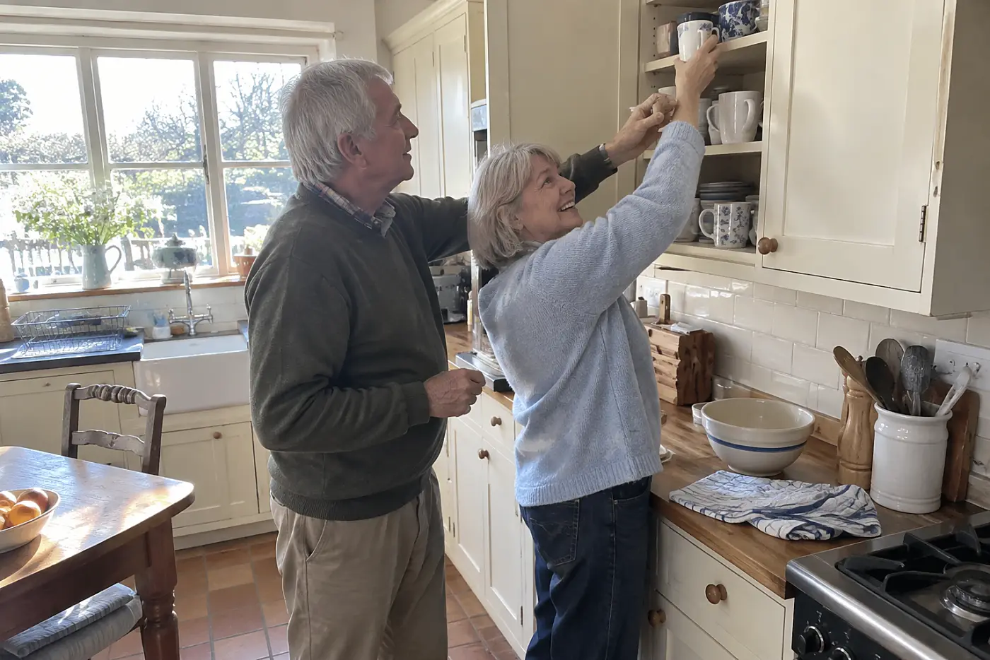 Older woman moving mugs from a high kitchen cupboard to a lower shelf.