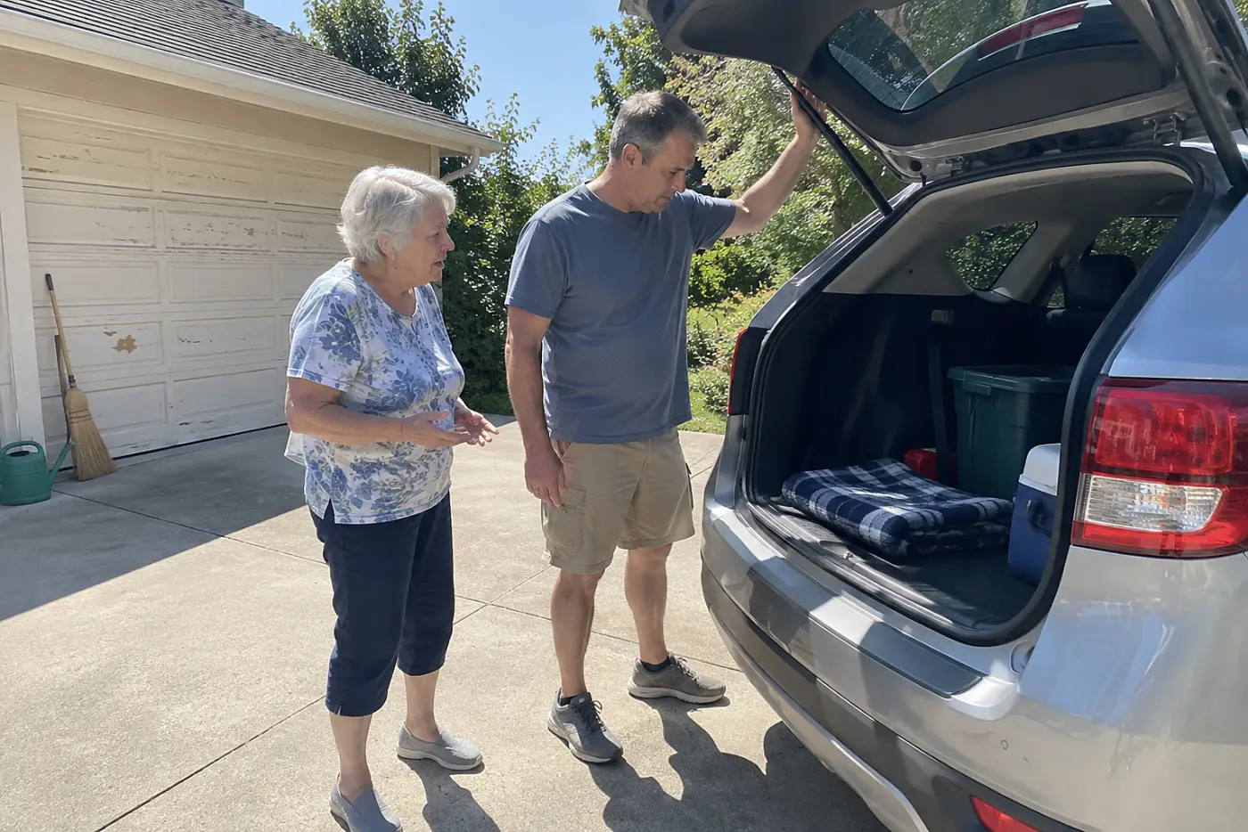 Mother and adult son talking beside a car parked in a driveway.