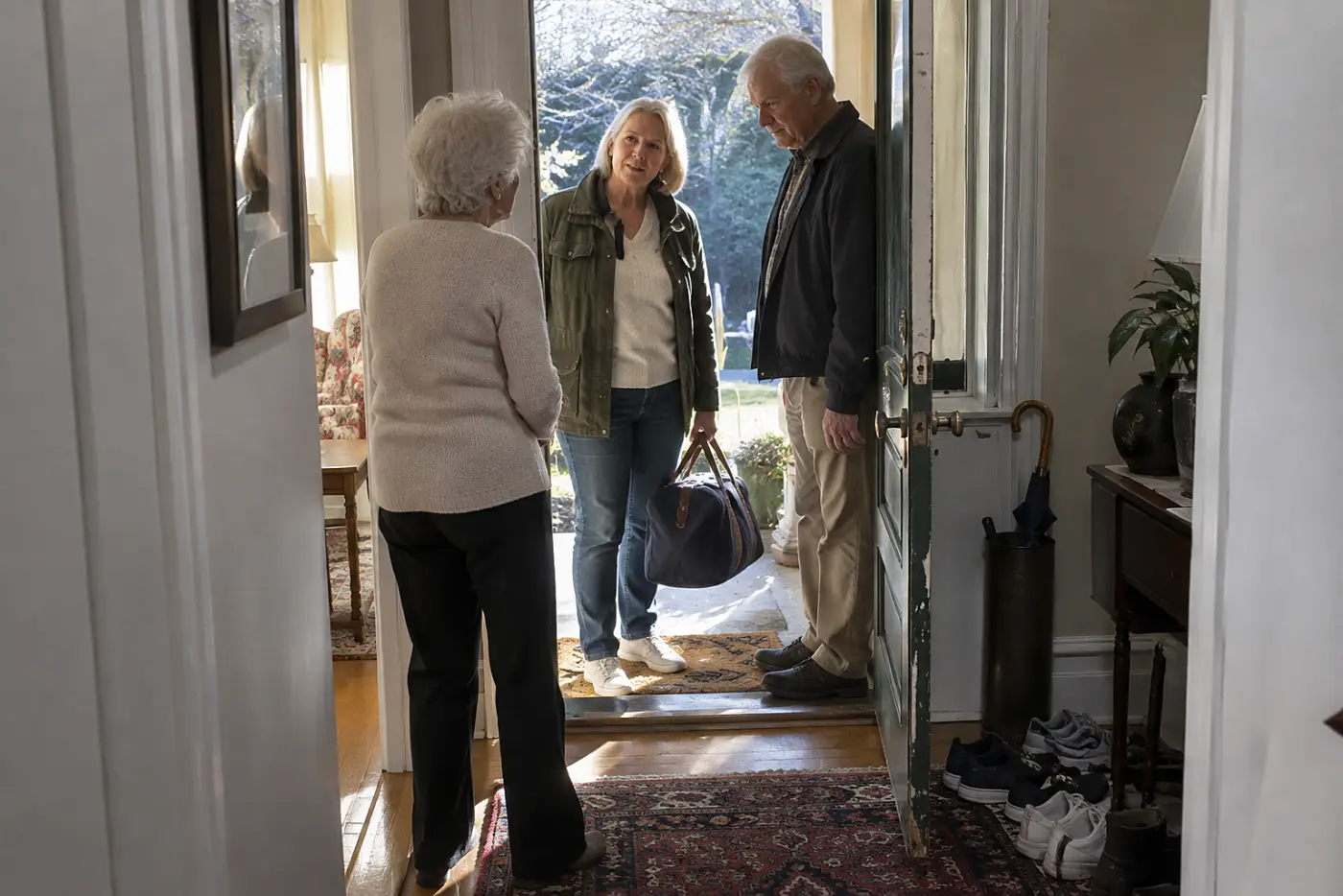 Adult daughter standing in her mother's doorway beside an unexpected guest.