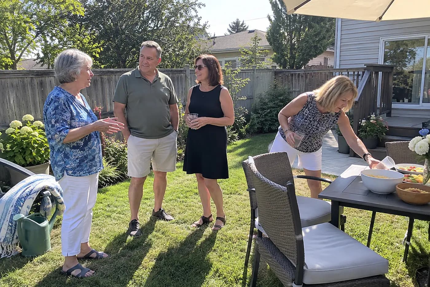 Older woman speaking with guests while her daughter stands nearby at a backyard party.