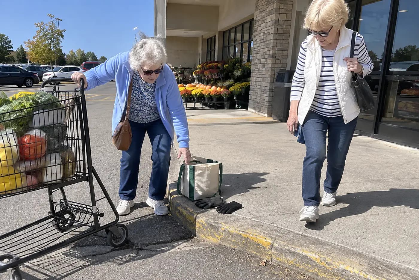 Older woman steps onto a curb outside a grocery store.