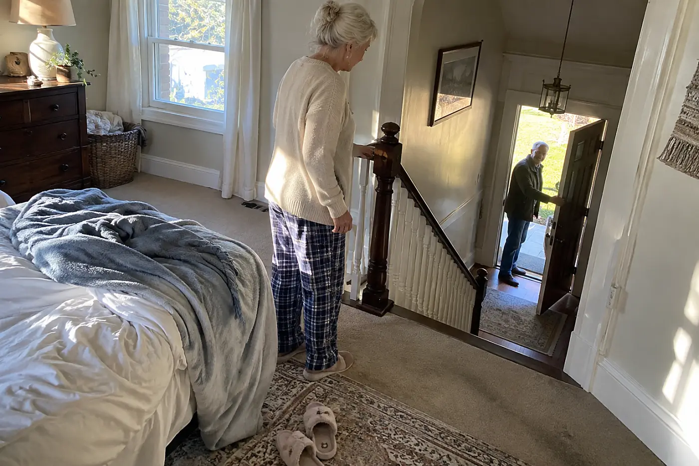 Older woman looks toward her front door from an upstairs bedroom.
