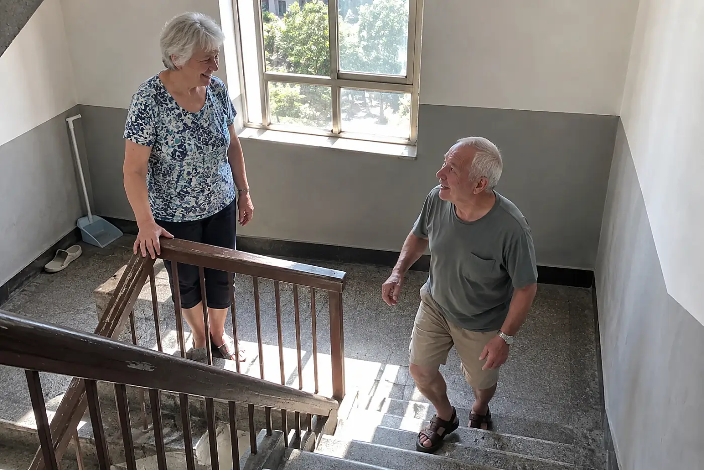 Older woman rests a hand on a staircase railing at the landing.