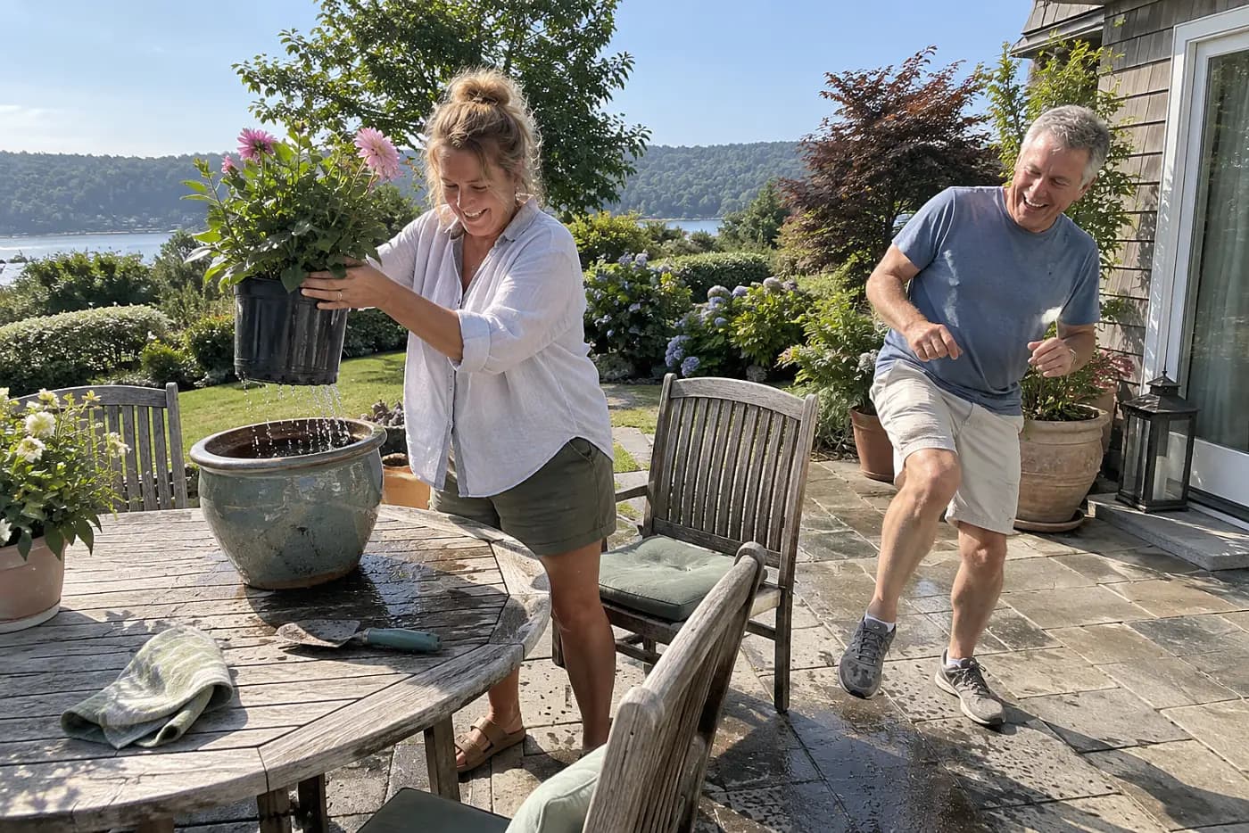 Woman lifting a plastic nursery pot from a water-filled ceramic pot on a patio table.