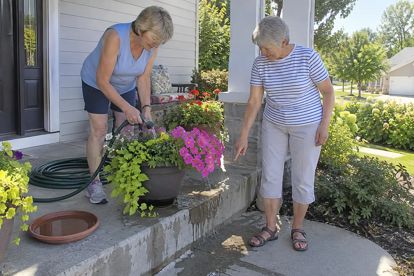 Woman holding a hose nozzle beneath petunia leaves on her porch.