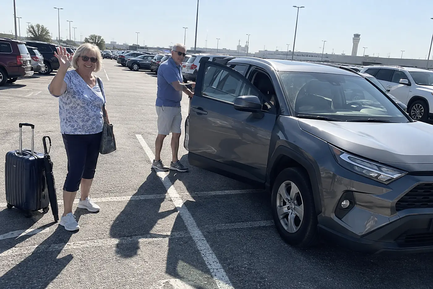 Older woman photographing a rental car in an airport parking lot.