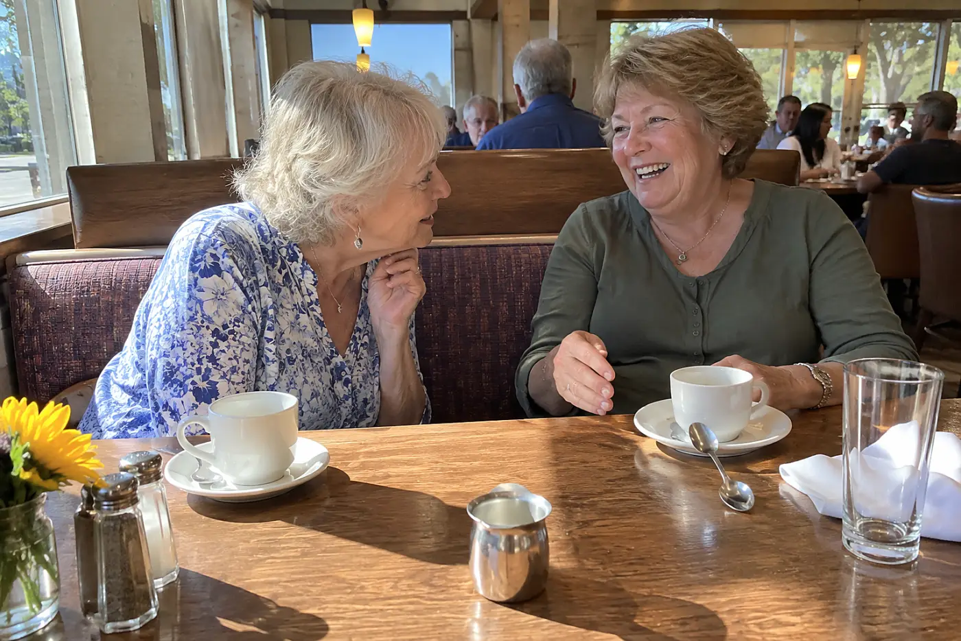Older woman leaning toward a friend at a restaurant table.