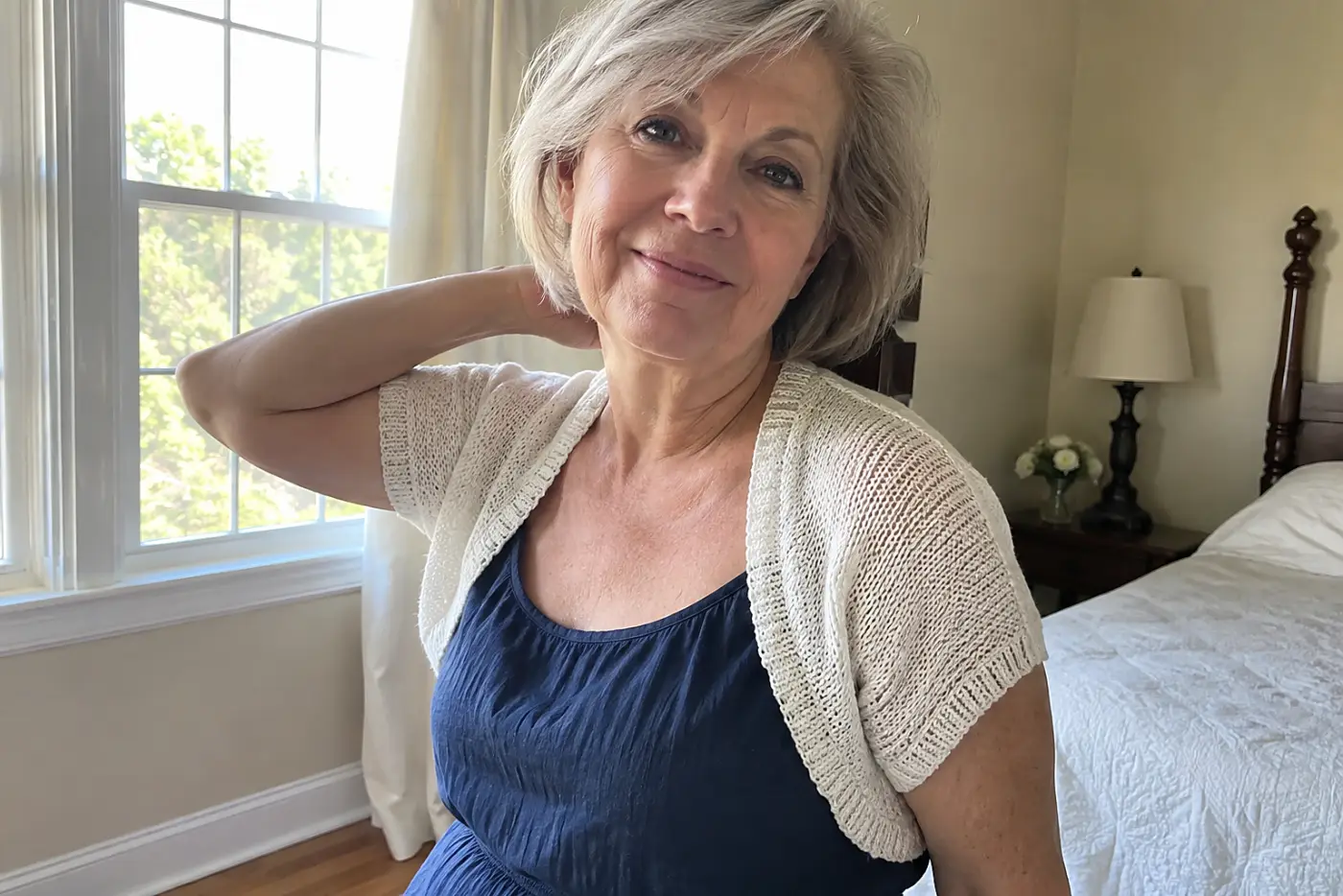A small knit shrug covers the shoulders of a woman in her sixties over a dress in her bedroom, centered and fully visible with no writing nearby.
