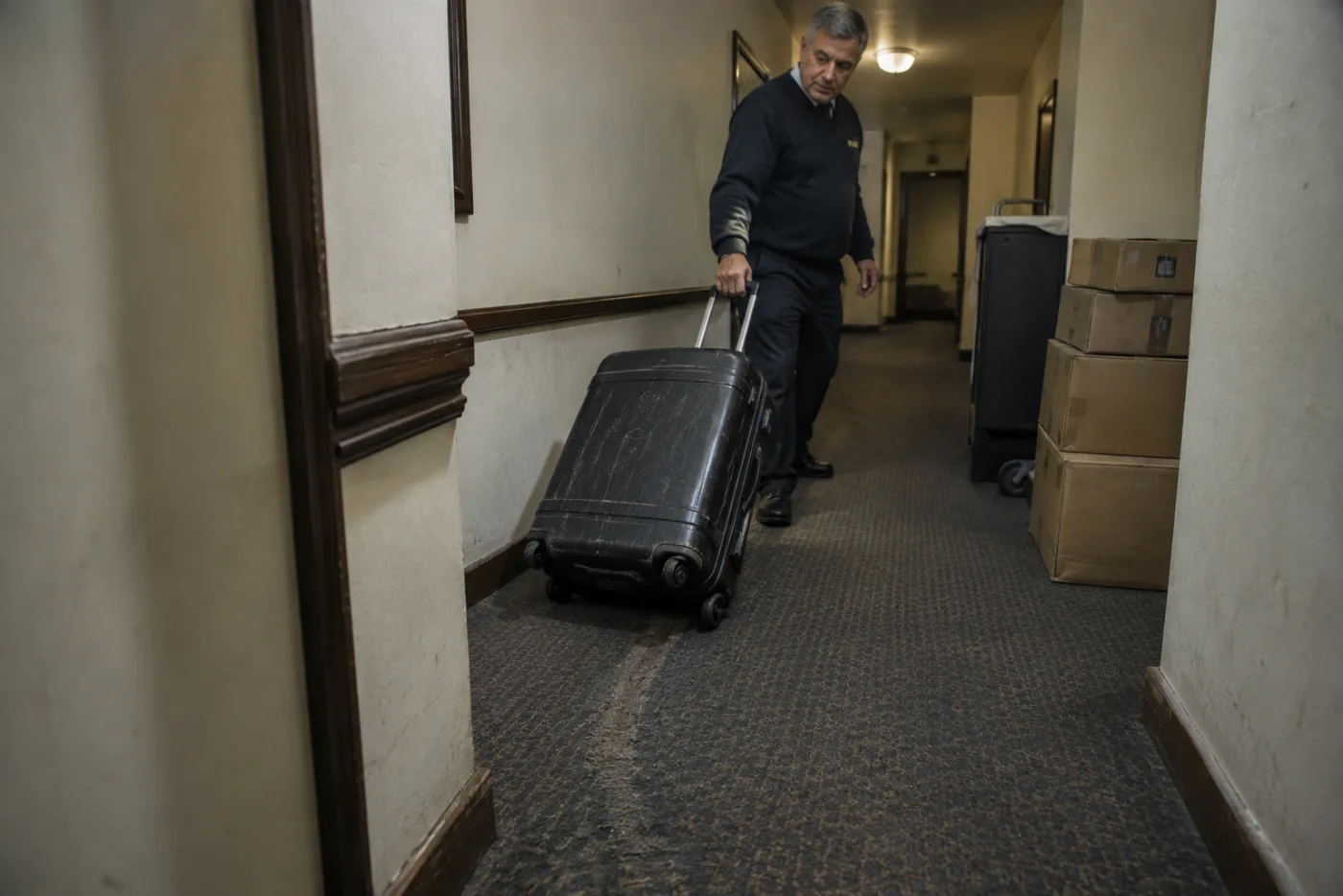 Steward drags a suitcase clear of a narrow ship hallway junction.
