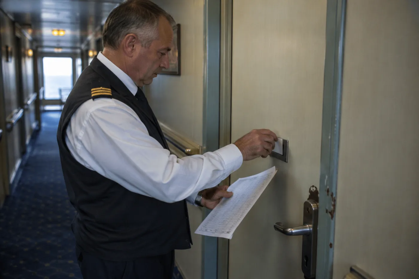 Steward tucks a dietary request card into a slot on a cabin door.