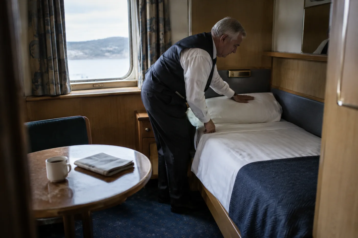 Steward turns down a single bed in a compact solo cabin.