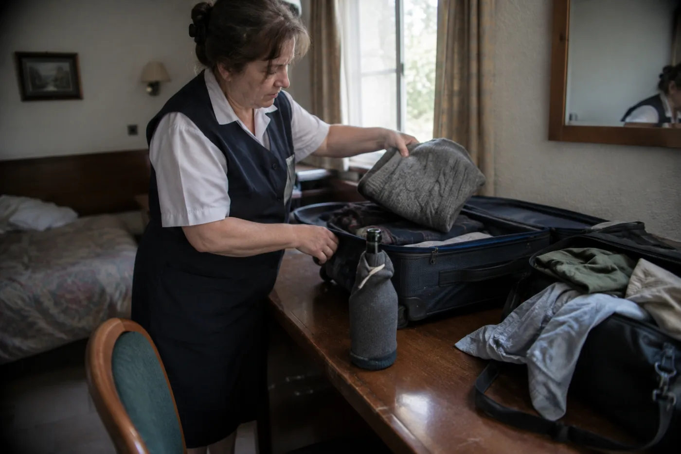 Steward lifts a sweater in a suitcase, revealing a hidden wrapped bottle.
