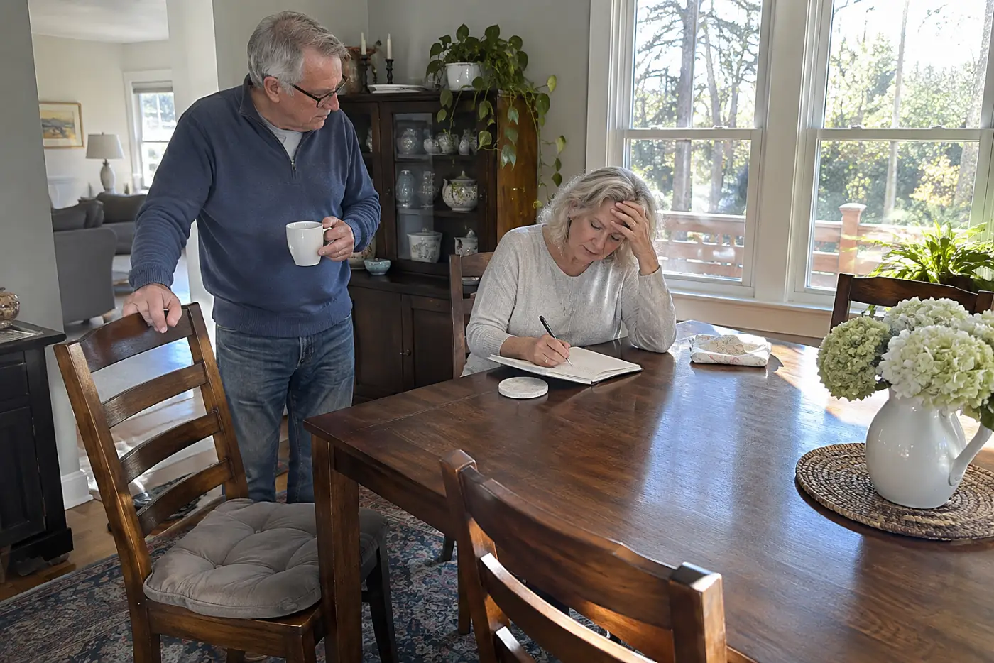 Older woman recording her sleep times in a notebook at her dining table.