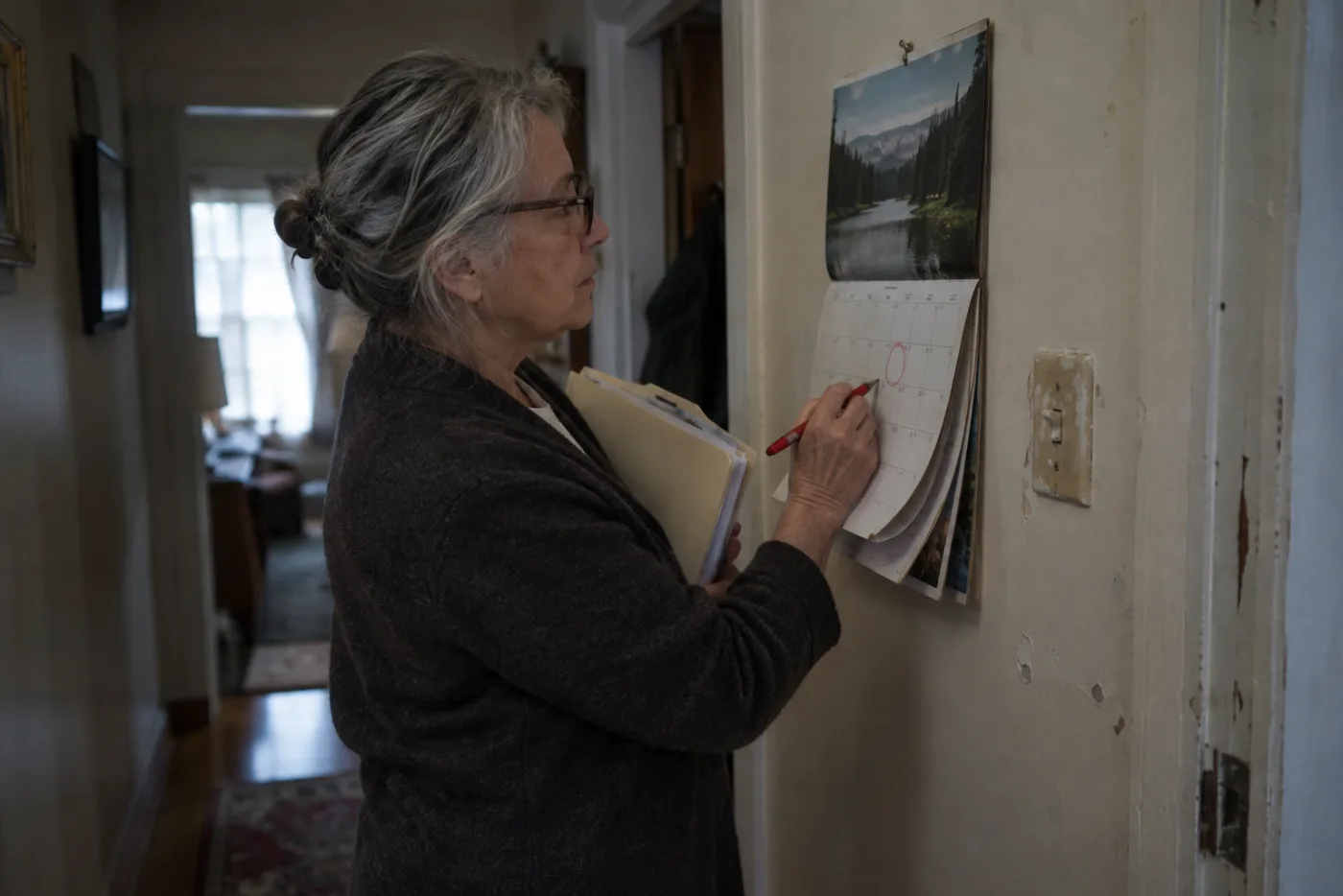Woman circling a birthday month on a wall calendar holding a folder of paperwork