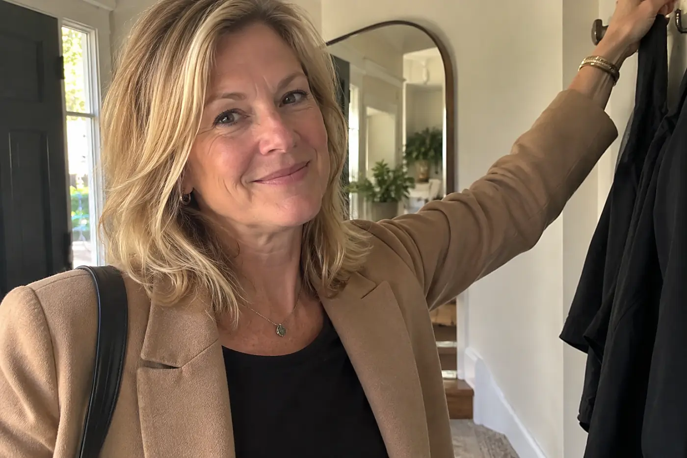 A blazer with room in the arms is centered on a woman over 50 reaching for a coat hook by her front door.