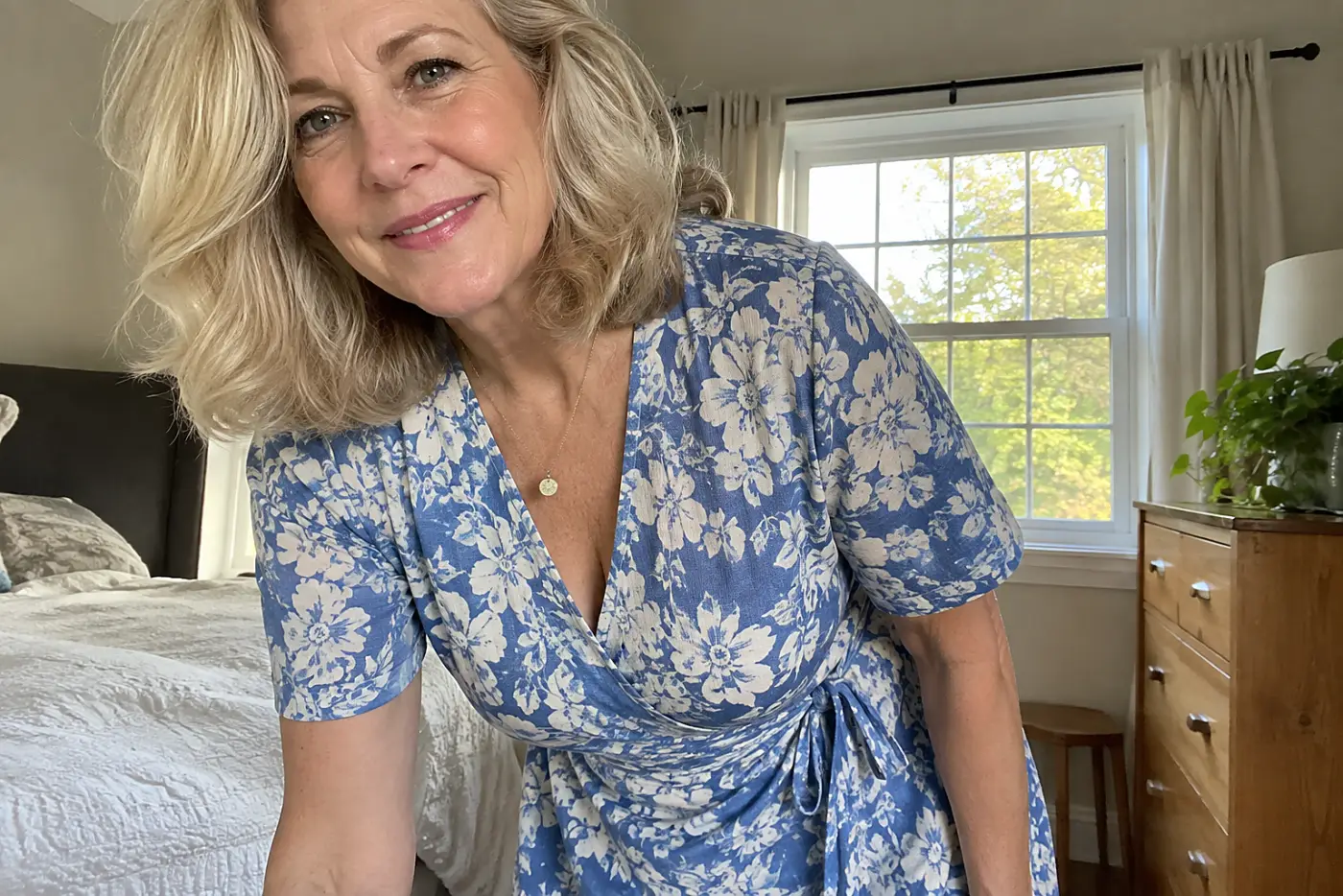 A wrap dress with a secure neckline is centered on a woman over 50 bending to pick up her bag at home.
