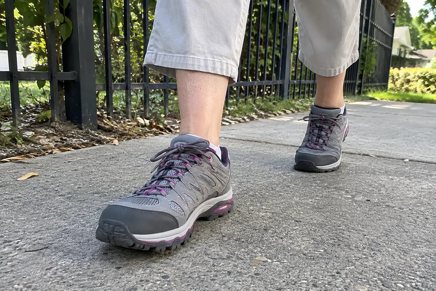 Shoes suited to a long walk are centered on the feet of a woman in her sixties crossing a neighborhood sidewalk.