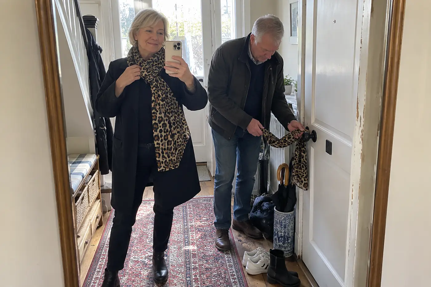 Older woman arranging a leopard-print scarf over her coat in a hallway mirror.