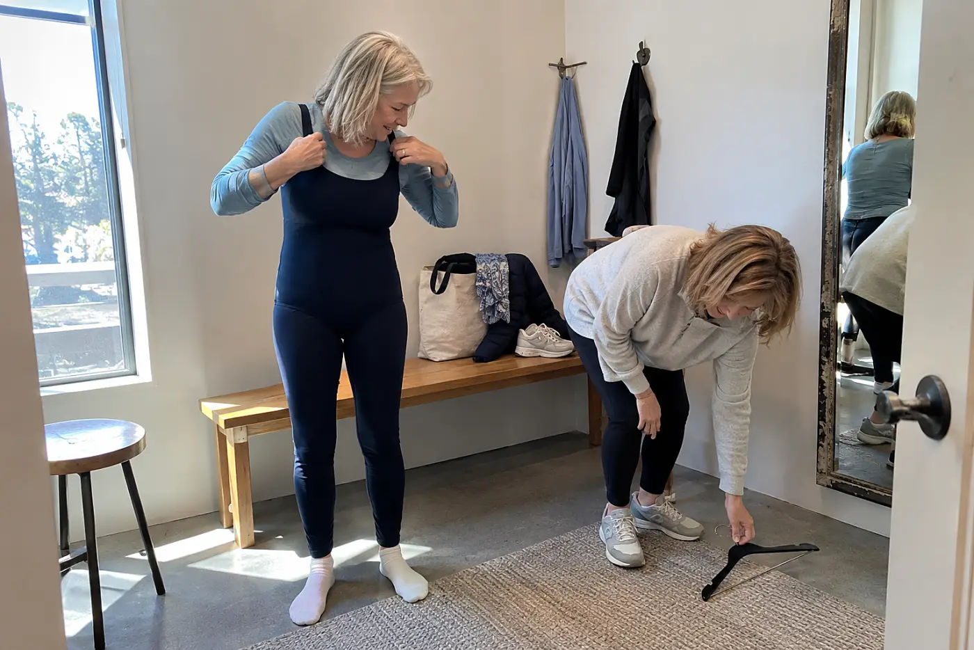 Older woman bending to check a swimsuit’s straps in a fitting room.