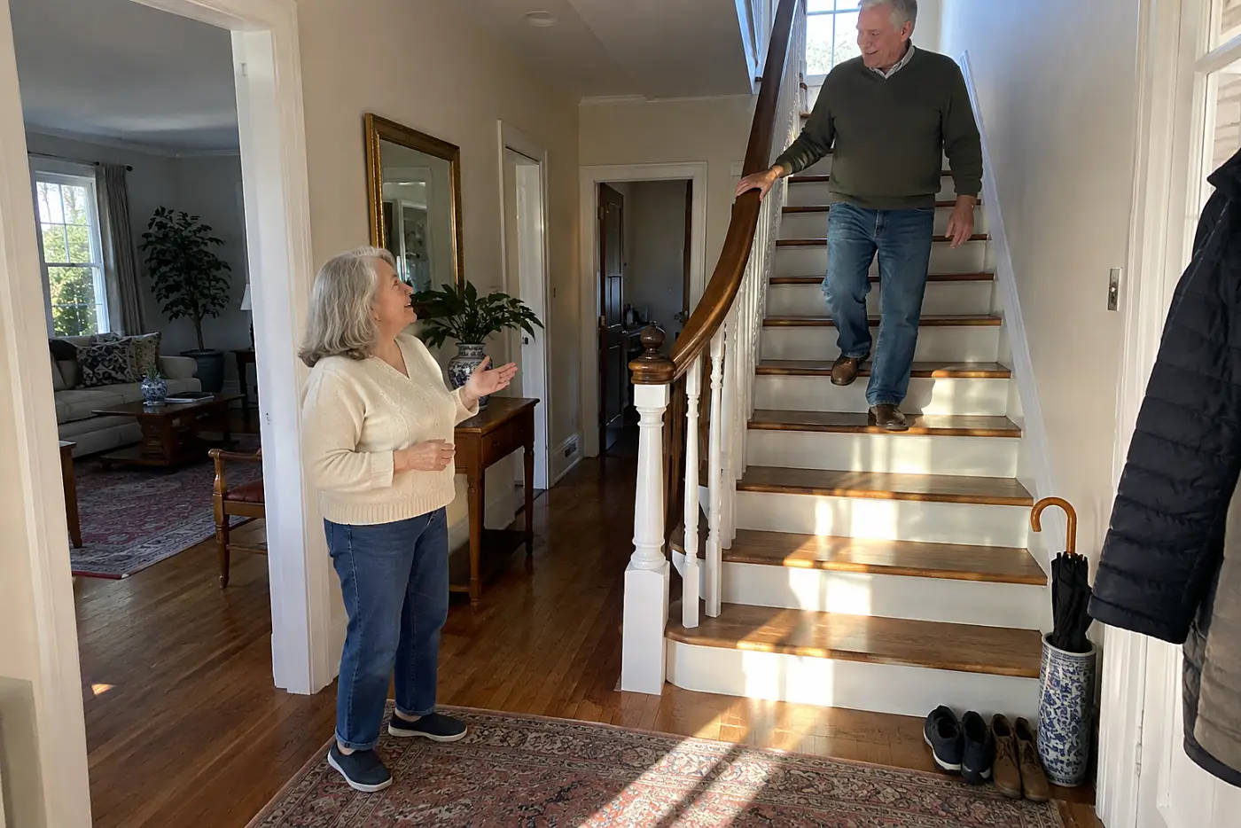 Older woman looking up toward the landing from the foot of her stairs.